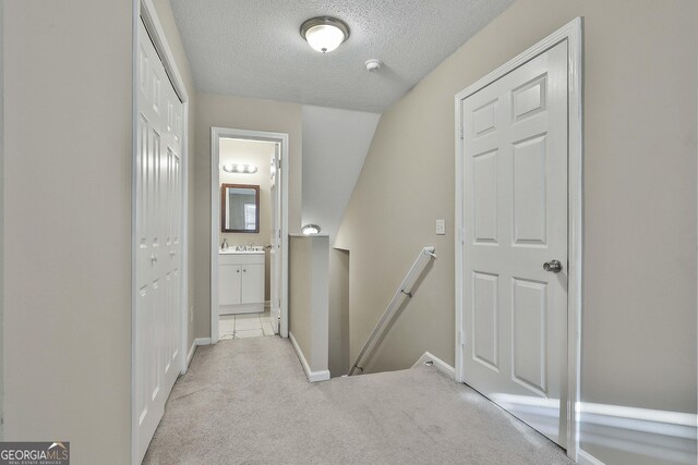 hall featuring light carpet, a textured ceiling, and vaulted ceiling