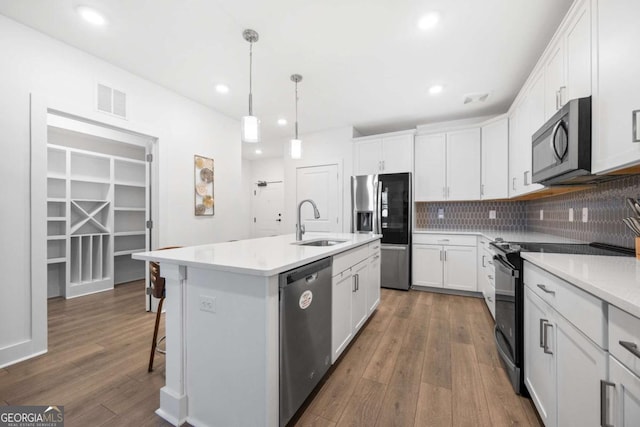 kitchen featuring pendant lighting, sink, stainless steel appliances, white cabinets, and a center island with sink