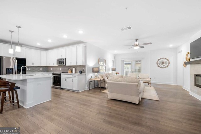 kitchen with stainless steel appliances, a kitchen island with sink, pendant lighting, and white cabinets