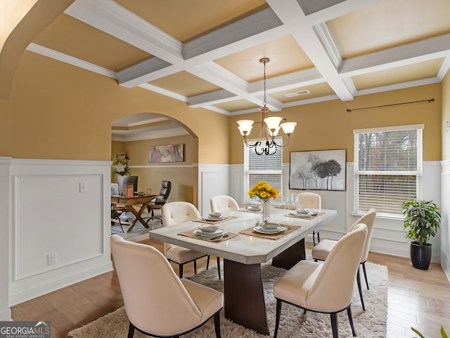 dining room with coffered ceiling, beamed ceiling, crown molding, a chandelier, and light wood-type flooring