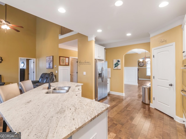 kitchen featuring a kitchen island with sink, white cabinets, sink, stainless steel fridge, and light stone countertops