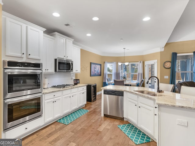 kitchen with white cabinetry, sink, hanging light fixtures, stainless steel appliances, and light hardwood / wood-style floors