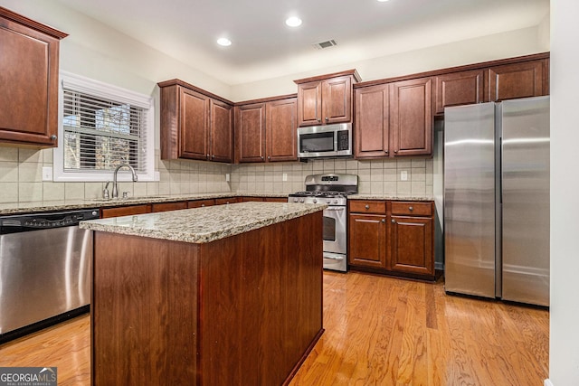 kitchen featuring light stone countertops, sink, appliances with stainless steel finishes, a kitchen island, and light wood-type flooring