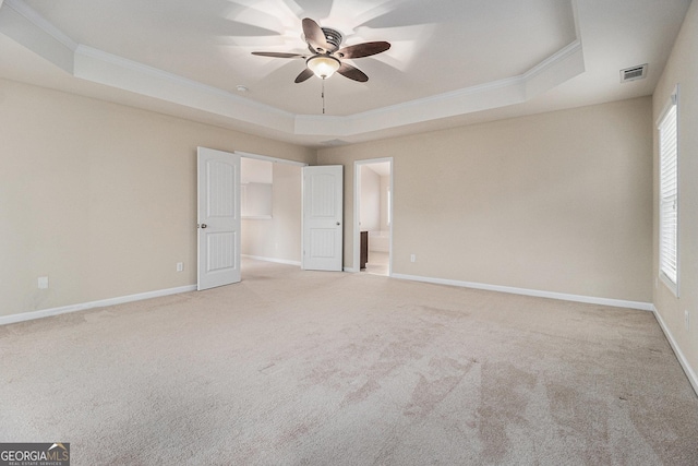 empty room featuring a raised ceiling, ceiling fan, light colored carpet, and ornamental molding