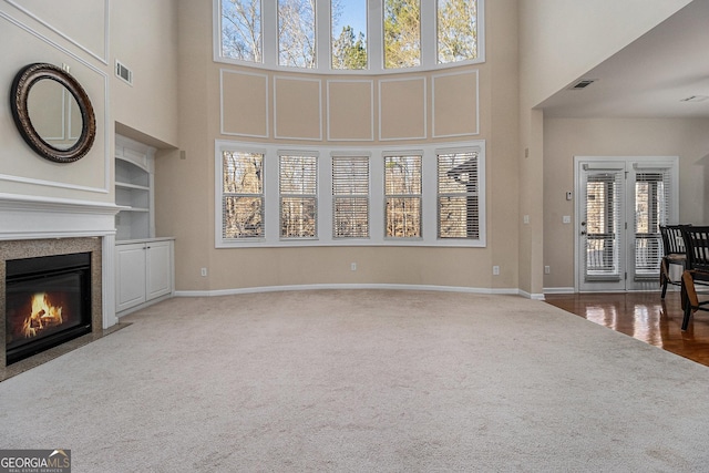 unfurnished living room featuring built in shelves, a towering ceiling, and dark carpet