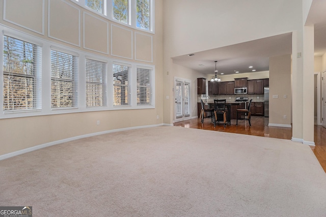 unfurnished living room featuring dark colored carpet, a healthy amount of sunlight, a high ceiling, and a notable chandelier