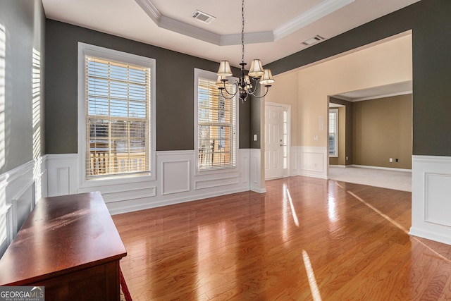 unfurnished dining area with hardwood / wood-style flooring, an inviting chandelier, ornamental molding, and a tray ceiling