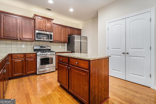 kitchen featuring appliances with stainless steel finishes, backsplash, a kitchen island, and light stone counters