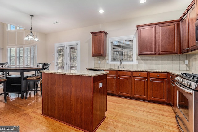 kitchen featuring light wood-type flooring, a kitchen island, decorative light fixtures, an inviting chandelier, and stainless steel range with gas cooktop