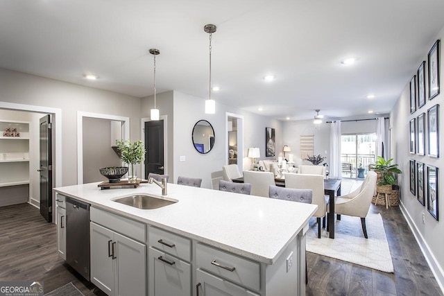 kitchen featuring dark wood-type flooring, stainless steel dishwasher, pendant lighting, a center island with sink, and sink