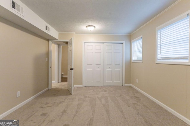 unfurnished bedroom featuring a closet, light colored carpet, a textured ceiling, and ornamental molding