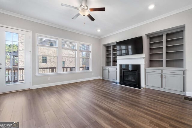 unfurnished living room with dark hardwood / wood-style floors, built in features, plenty of natural light, and crown molding