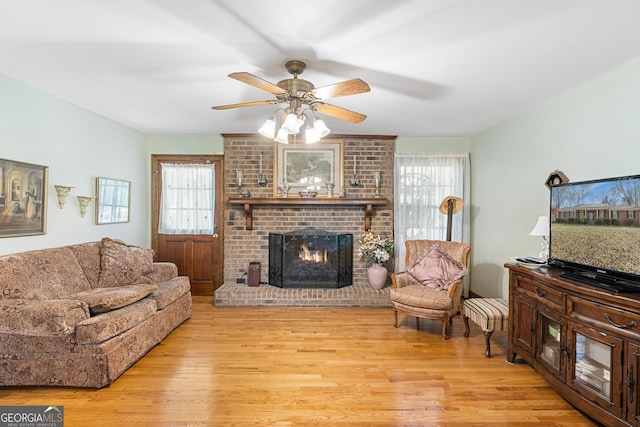 living room with ceiling fan, light hardwood / wood-style floors, and a brick fireplace