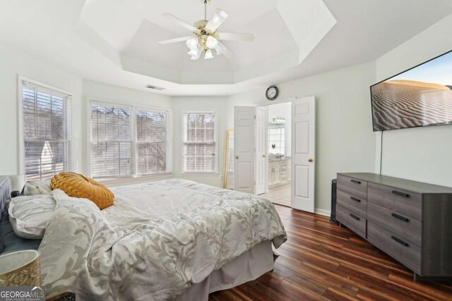 bedroom with ceiling fan, dark hardwood / wood-style floors, a raised ceiling, and ensuite bath