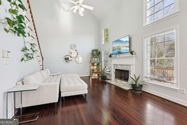 living room with a towering ceiling, hardwood / wood-style flooring, a healthy amount of sunlight, and a premium fireplace