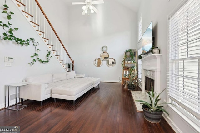 living room featuring a fireplace, a high ceiling, dark hardwood / wood-style flooring, and ceiling fan