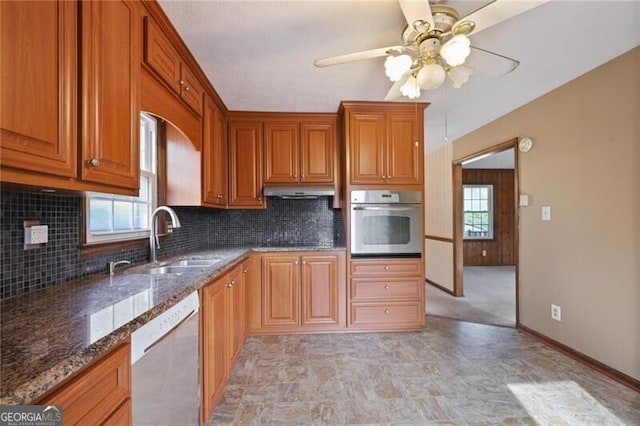 kitchen with backsplash, stainless steel appliances, ceiling fan, sink, and dark stone countertops