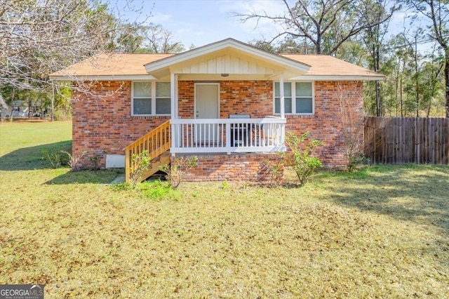 ranch-style home featuring a porch, a front yard, brick siding, and fence