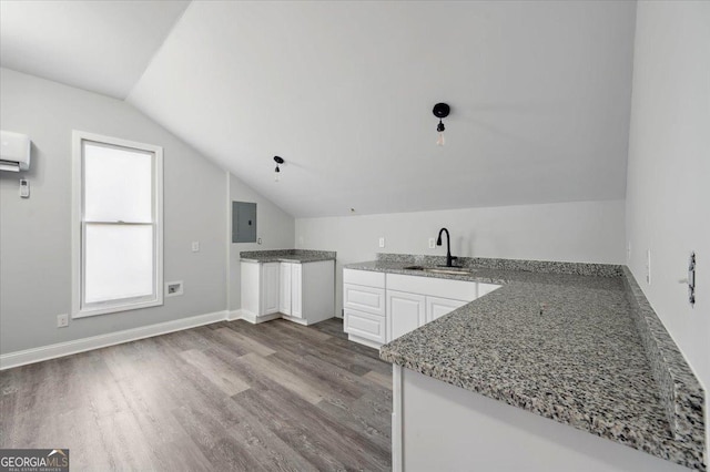 kitchen featuring electric panel, white cabinets, wood finished floors, vaulted ceiling, and a sink