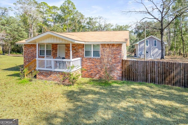 view of front of property featuring covered porch, brick siding, fence, and a front lawn