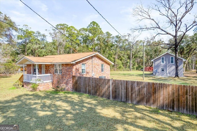 view of side of property featuring covered porch, fence, a lawn, and brick siding