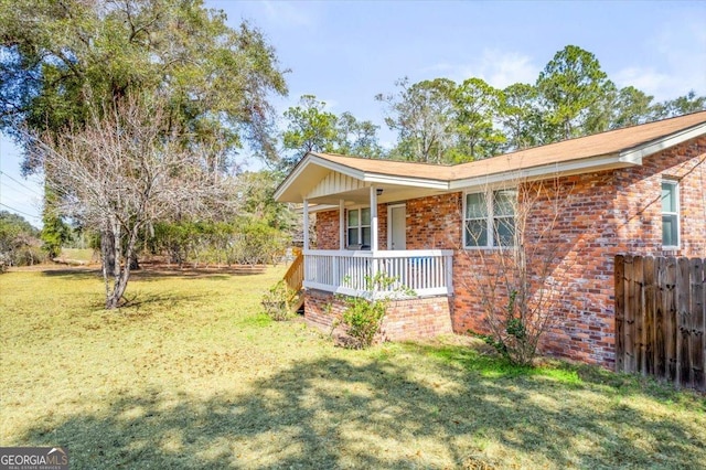 view of home's exterior with a yard, fence, a porch, and brick siding