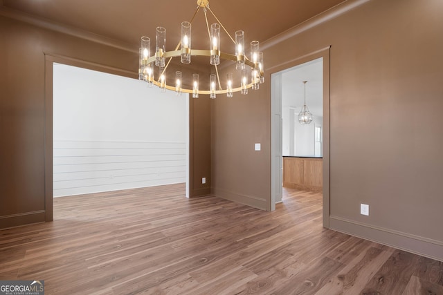 unfurnished dining area featuring ornamental molding, a chandelier, baseboards, and wood finished floors