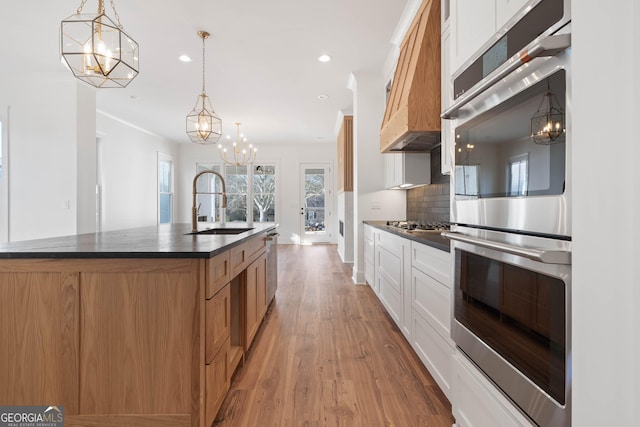 kitchen with dark countertops, stainless steel appliances, white cabinetry, pendant lighting, and a sink