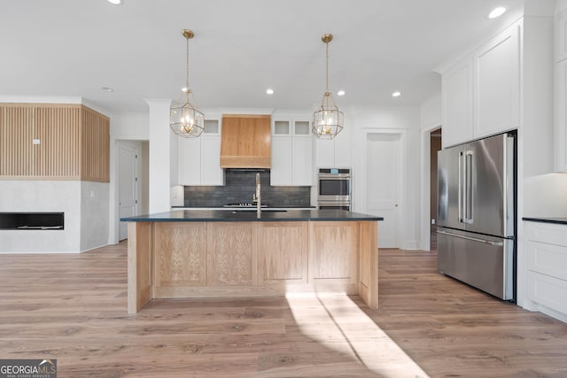 kitchen with a center island with sink, light wood finished floors, appliances with stainless steel finishes, glass insert cabinets, and white cabinets