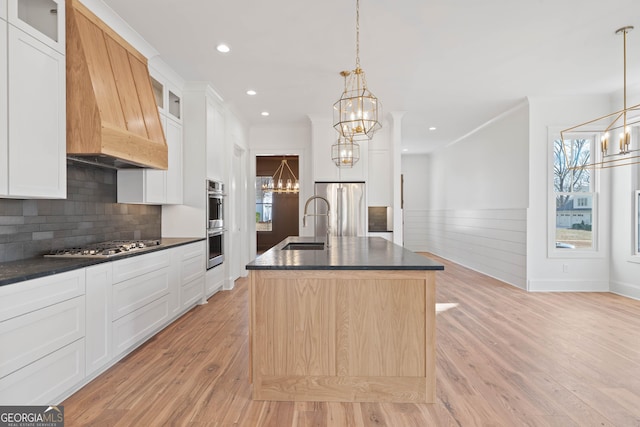 kitchen with dark countertops, an inviting chandelier, a center island with sink, and glass insert cabinets