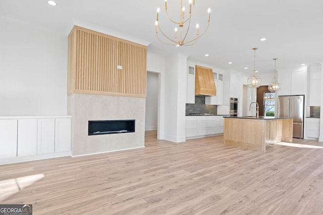 kitchen with a kitchen island with sink, stainless steel appliances, white cabinets, open floor plan, and custom exhaust hood