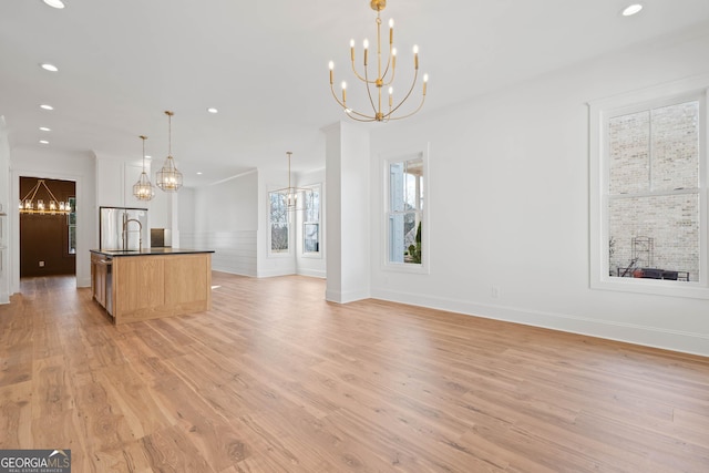 kitchen featuring decorative light fixtures, light wood finished floors, open floor plan, an island with sink, and a chandelier