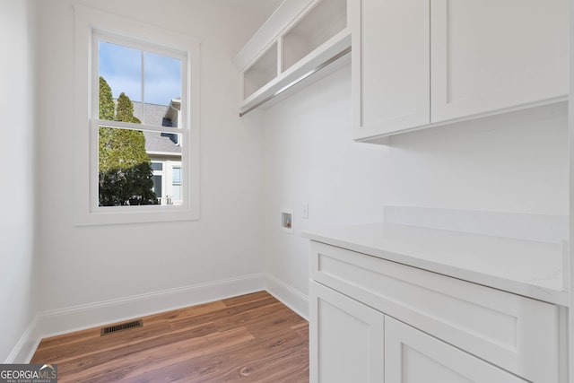 laundry room featuring cabinet space, baseboards, visible vents, and wood finished floors
