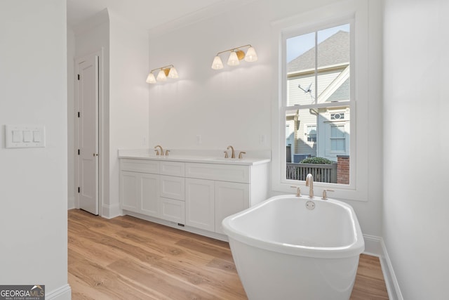 full bath with wood finished floors, a sink, baseboards, a soaking tub, and double vanity