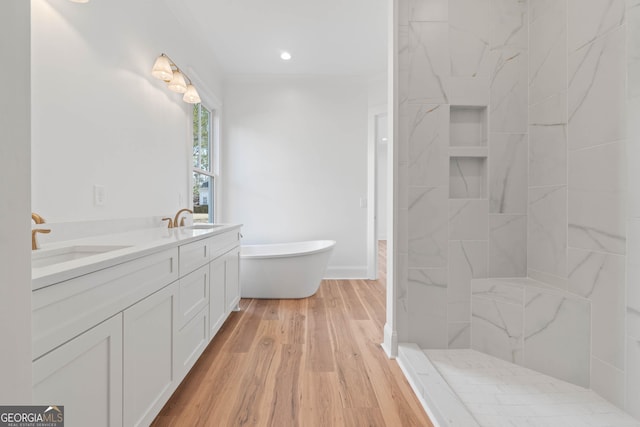 bathroom with double vanity, a freestanding bath, a sink, and wood finished floors