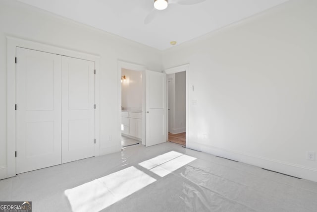 unfurnished bedroom featuring light carpet, baseboards, ceiling fan, ensuite bathroom, and a closet