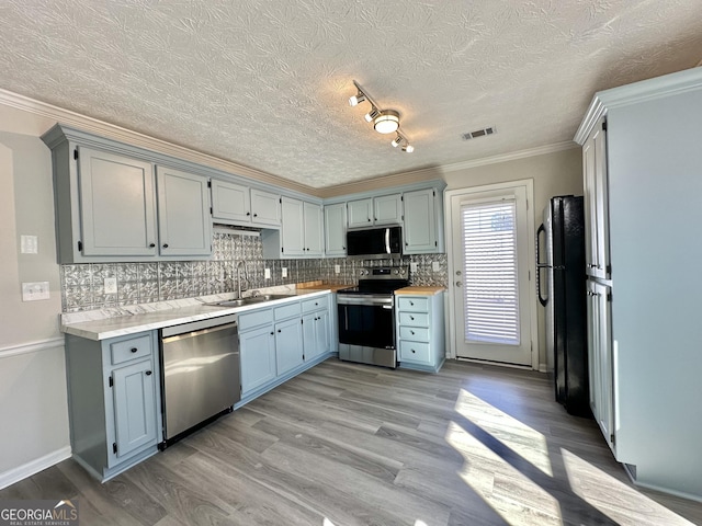 kitchen featuring appliances with stainless steel finishes, tasteful backsplash, sink, ornamental molding, and light wood-type flooring