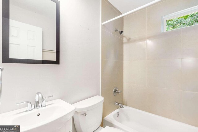 full bathroom featuring tiled shower / bath combo, toilet, and sink