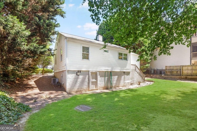 rear view of property with central air condition unit and a lawn