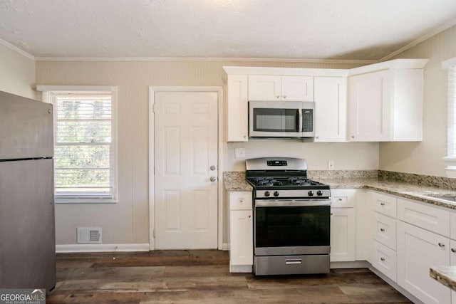 kitchen with light stone countertops, white cabinetry, ornamental molding, and appliances with stainless steel finishes