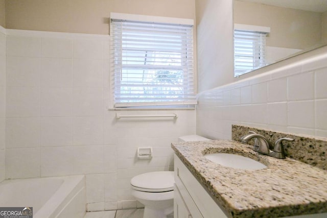 bathroom with a washtub, vanity, tile walls, and toilet