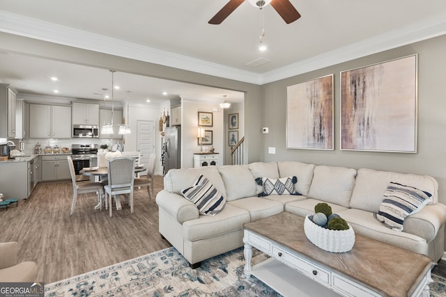 living room with ceiling fan, sink, ornamental molding, and light wood-type flooring