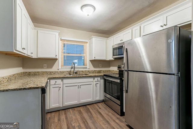 kitchen with light stone counters, stainless steel appliances, dark wood-type flooring, sink, and white cabinets