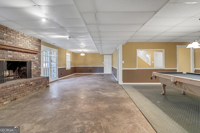 game room with a brick fireplace, a drop ceiling, concrete floors, and french doors