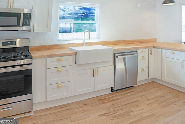 kitchen featuring white cabinets, butcher block countertops, appliances with stainless steel finishes, light wood-type flooring, and a sink