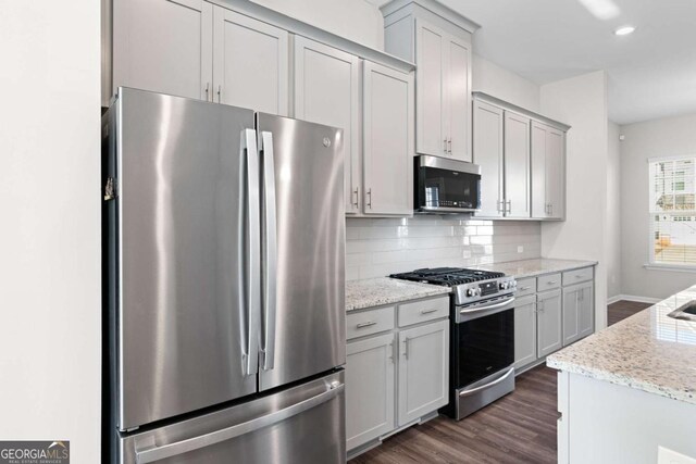 kitchen featuring gray cabinetry, backsplash, light stone counters, and stainless steel appliances