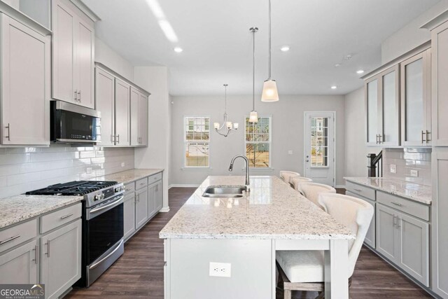 kitchen featuring a kitchen island with sink, a kitchen breakfast bar, sink, gray cabinets, and appliances with stainless steel finishes