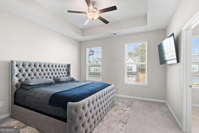 bedroom with light carpet, a raised ceiling, and ceiling fan