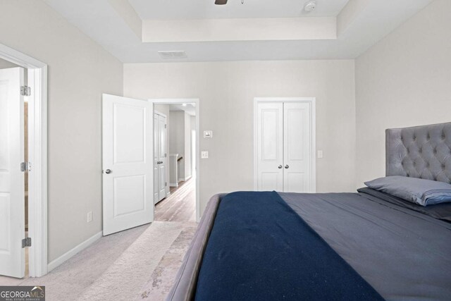 bedroom featuring a raised ceiling, light carpet, a closet, and ceiling fan