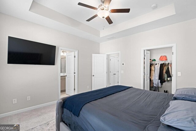 carpeted bedroom featuring connected bathroom, a tray ceiling, and ceiling fan